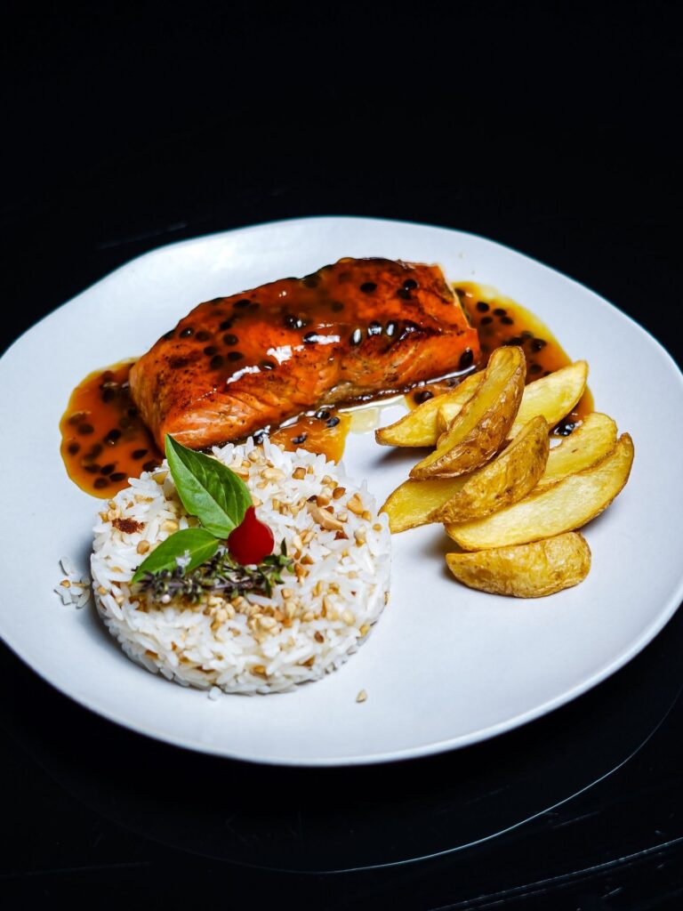 A gourmet dish featuring glazed salmon, seasoned rice, and golden potato wedges.